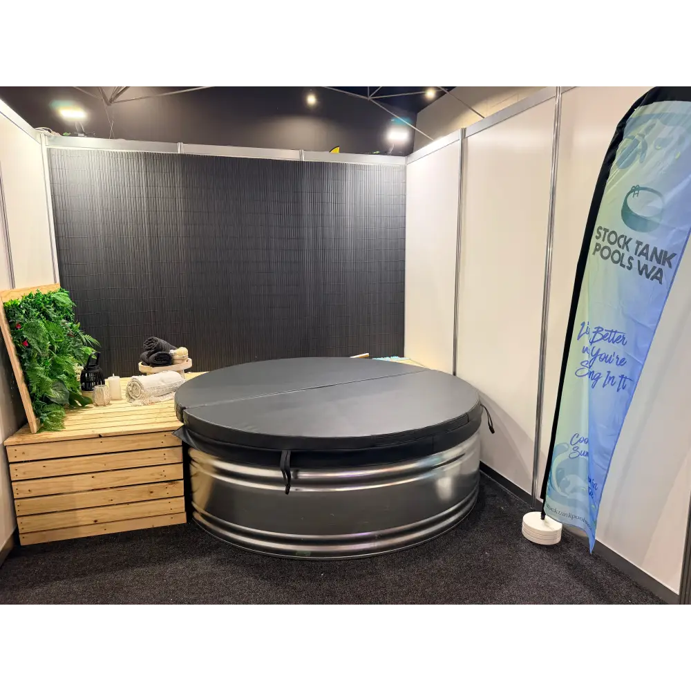 A circular metal stock tank with a dark gray fitted cover, displayed inside a booth at the home expo perth with vertical banner reading Stock Tank Pools Wa.
