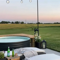 Outdoor stock tank pool on a patio with lounge chairs, string lights, and a large grassy field in the background at dusk in regional australia