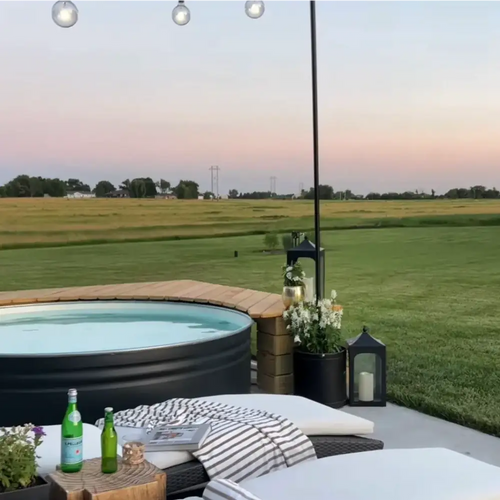 Outdoor stock tank pool on a patio with lounge chairs, string lights, and a large grassy field in the background at dusk in regional australia
