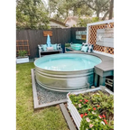 A round galvanized steel outdoor pool with light blue water, set in a backyard with a wooden fence, patio seating, and garden plants landscape design