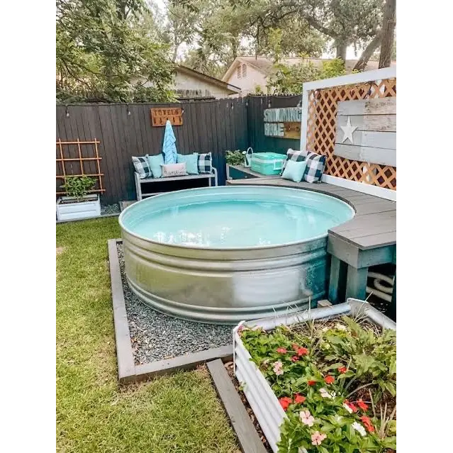 A round galvanized steel outdoor pool with light blue water, set in a backyard with a wooden fence, patio seating, and garden plants landscape design